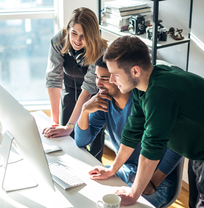 Sales team smiling and collaborating around a desktop computer in a bright, modern office